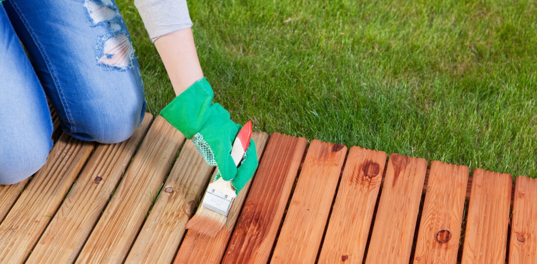 Person wearing gloves using a brush to apply stain to a wooden deck