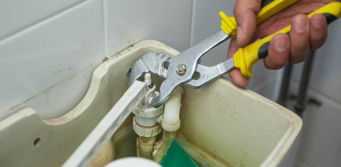 Close-up of a hand using pliers inside a toilet water tank